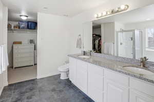 Full bath with a walk in closet, a stall shower, double vanity, and dark tile patterned flooring