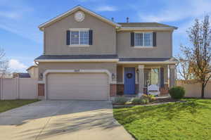 Traditional-style house with brick siding, covered porch, an attached garage, concrete driveway, and stucco siding