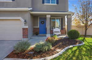 Entrance to property with brick siding, a porch, a garage, and stucco siding