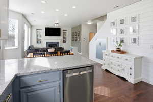 Kitchen with light stone counters, stainless steel dishwasher, a fireplace, dark wood-style floors, and recessed lighting