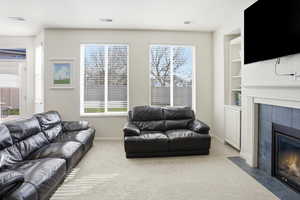 Carpeted living area with a tile fireplace and built in features