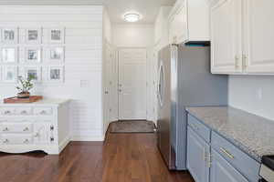 Kitchen featuring dark wood-style flooring, white cabinets, light stone countertops, and freestanding refrigerator