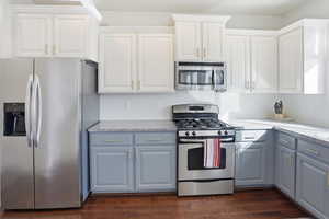 Kitchen with appliances with stainless steel finishes, white cabinetry, light stone countertops, and dark wood-style floors