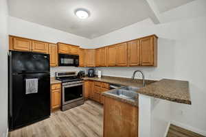 Kitchen with brown cabinetry, black appliances, a peninsula, and light wood-style flooring