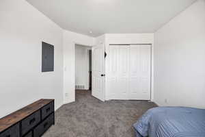 Bedroom with electric panel, dark colored carpet, and a closet
