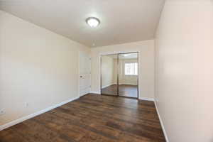 Unfurnished bedroom with dark wood-style floors and a closet