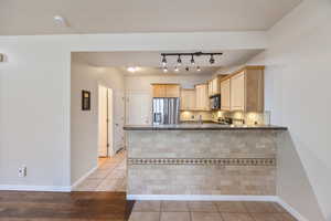 Kitchen featuring light brown cabinets, light tile patterned floors, stainless steel fridge with ice dispenser, a peninsula, and backsplash