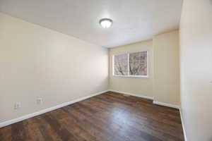 Spare room with dark wood-type flooring and baseboards