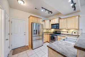 Kitchen featuring light brown cabinetry, stainless steel appliances, light tile patterned floors, dark countertops, and tasteful backsplash