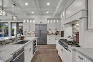 Kitchen with light stone countertops, appliances with stainless steel finishes, hanging light fixtures, beamed ceiling, and white cabinets