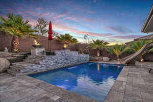 Pool at dusk with a fenced backyard, a patio area, and a water slide