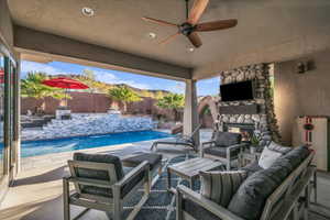 Fenced backyard with an outdoor living space with a fireplace, a patio, and a ceiling fan