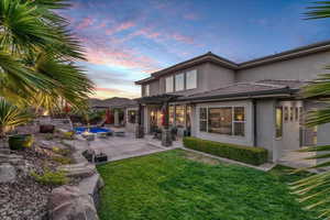 Back of house at dusk with stucco siding, a pergola, a lawn, an outdoor pool, and a patio
