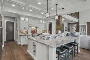 Kitchen featuring white cabinets, a kitchen breakfast bar, light stone counters, open floor plan, and coffered ceiling