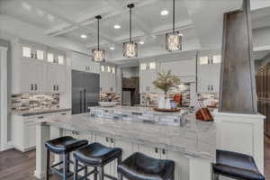 Kitchen featuring backsplash, a kitchen breakfast bar, glass insert cabinets, white cabinetry, and coffered ceiling