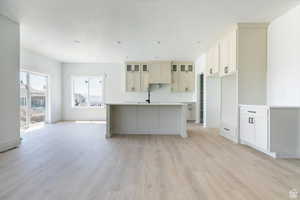 Kitchen featuring a center island with sink, light wood finished floors, light countertops, open floor plan, and glass insert cabinets
