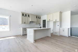Kitchen with custom range hood, light wood finished floors, a center island with sink, a breakfast bar area, and light stone countertops
