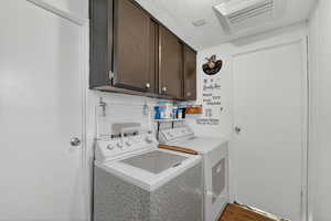 Laundry room with cabinet space, washer and dryer, a textured ceiling, and wood finished floors