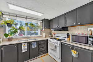 Kitchen featuring dark cabinets, white gas range, stainless steel microwave, light countertops, and decorative backsplash