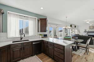 Kitchen featuring dark brown cabinetry, open floor plan, dishwashing machine, hanging light fixtures, and light wood-style floors