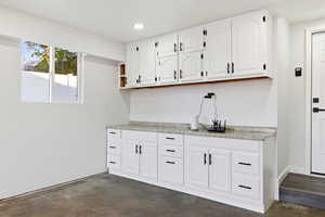 Kitchen featuring white cabinets, concrete flooring, light stone countertops, recessed lighting, and open shelves
