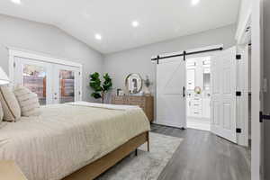 Bedroom with a barn door, wood finished floors, access to outside, vaulted ceiling, and french doors