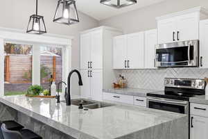 Kitchen featuring stainless steel appliances, light stone countertops, white cabinets, and decorative light fixtures