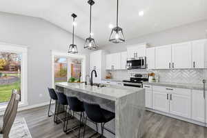 Kitchen with a kitchen bar, white cabinets, light stone countertops, stainless steel appliances, and decorative light fixtures
