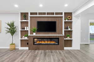 Unfurnished living room featuring recessed lighting, wood finished floors, a glass covered fireplace, and ornamental molding