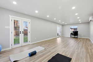 Unfurnished living room featuring french doors, recessed lighting, light wood-style flooring, a desk, and a wall mounted air conditioner
