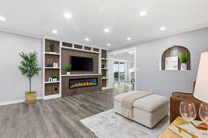 Living area featuring built in features, light wood finished floors, recessed lighting, a glass covered fireplace, and ornamental molding