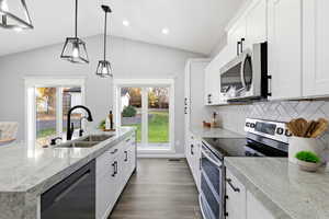 Kitchen featuring stainless steel appliances, white cabinetry, decorative backsplash, hanging light fixtures, and lofted ceiling