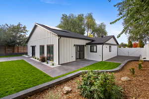 Back of house with a fenced backyard, roof with shingles, a gate, board and batten siding, and roof mounted solar panels