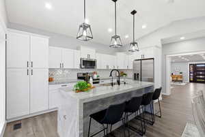 Kitchen with a breakfast bar area, tasteful backsplash, stainless steel appliances, light stone counters, and a center island with sink