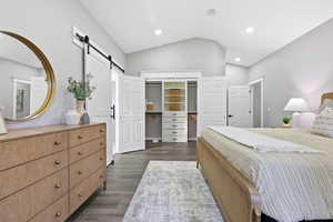 Bedroom with vaulted ceiling, a barn door, wood finished floors, and recessed lighting