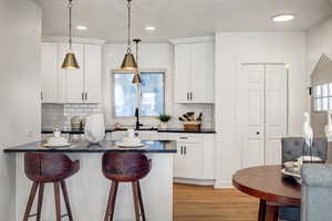 Kitchen with a breakfast bar, tasteful backsplash, decorative light fixtures, light wood-style floors, and white cabinets