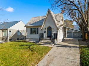 View of front of house with an outdoor structure, a front yard, driveway, and a shingled roof