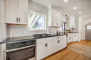 Kitchen featuring appliances with stainless steel finishes, white cabinetry, decorative light fixtures, light wood finished floors, and dark stone countertops