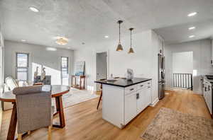 Kitchen featuring white cabinets, pendant lighting, a kitchen breakfast bar, dark stone countertops, and a textured ceiling