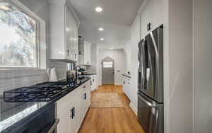 Kitchen with stainless steel appliances, white cabinetry, light wood-type flooring, decorative backsplash, and recessed lighting