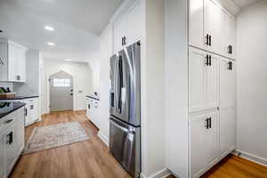 Kitchen featuring stainless steel fridge with ice dispenser, white cabinetry, light wood-style flooring, tasteful backsplash, and recessed lighting