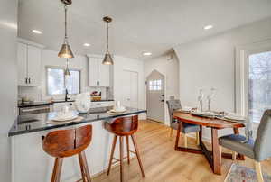 Kitchen featuring a breakfast bar, dark stone counters, white cabinetry, tasteful backsplash, and hanging light fixtures