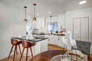 Kitchen featuring hanging light fixtures, a breakfast bar, light wood-type flooring, dark stone countertops, and backsplash