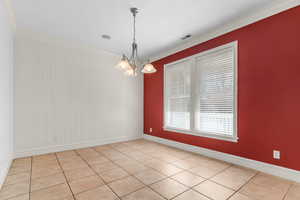 Empty room with ornamental molding, light tile patterned flooring, and a chandelier
