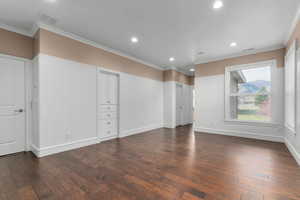 Empty room featuring ornamental molding, dark wood-style flooring, recessed lighting, and wainscoting