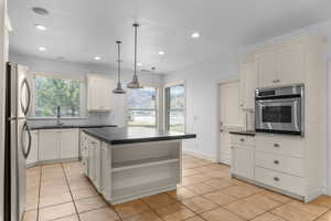 Kitchen with dark countertops, stainless steel appliances, hanging light fixtures, a kitchen island, and open shelves
