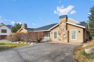 View of front facade featuring a chimney, roof with shingles, covered porch, and asphalt driveway