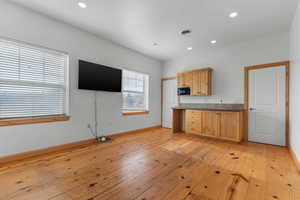 Kitchen featuring dark countertops, light wood-type flooring, recessed lighting, light brown cabinetry, and black microwave