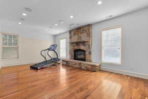 Exercise area with a fireplace, light wood-type flooring, healthy amount of natural light, and recessed lighting