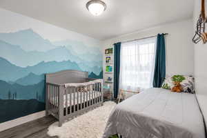 Bedroom featuring an accent wall, wood finished floors, and a nursery area